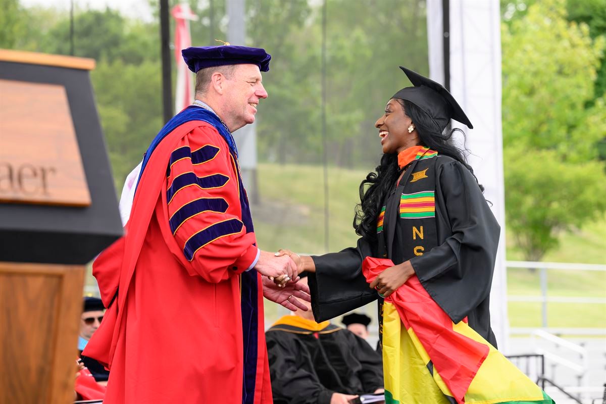 President Schmidt shakes hand with undergraduate female student crossing stage.