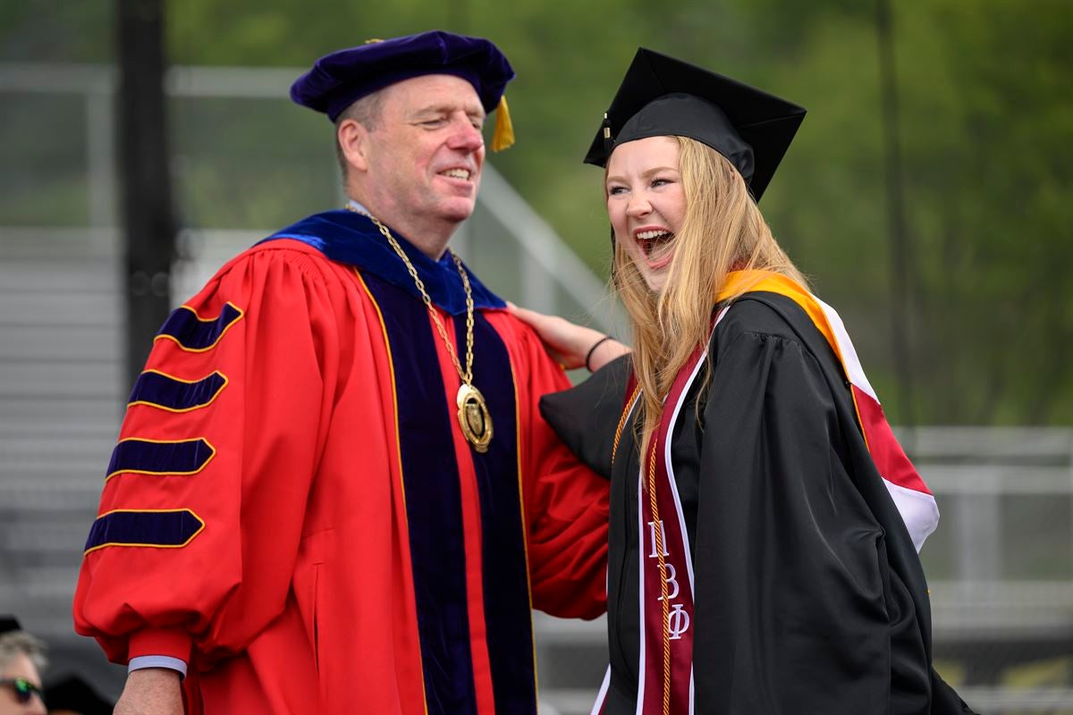 President Schmidt laughs with undergraduate female student crossing stage.