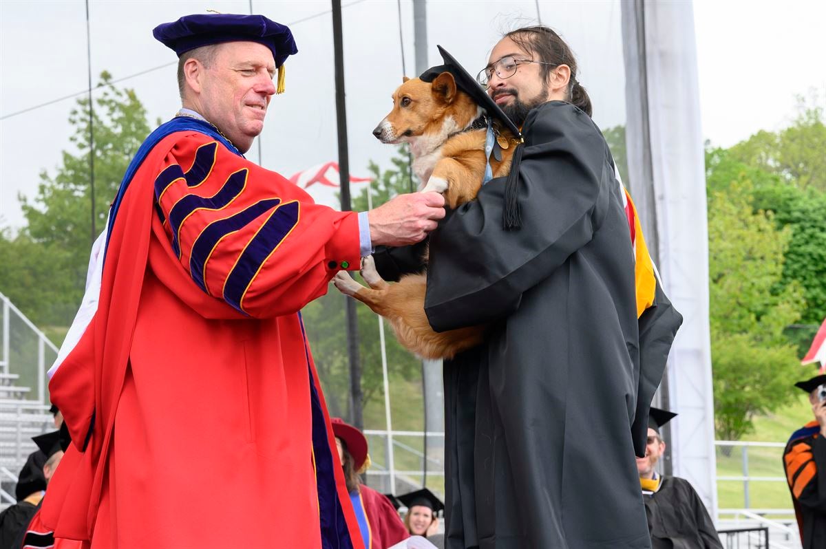 President Schmidt shakes hands with undergraduate male student and shakes his dog’s paw.