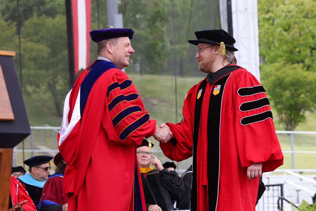 President Schmidt shakes hands with male doctoral graduate student crossing stage at Commencement.