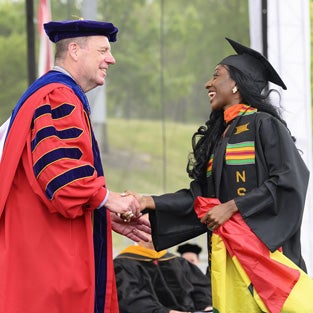 President Schmidt shakes hand with undergraduate female student crossing stage.