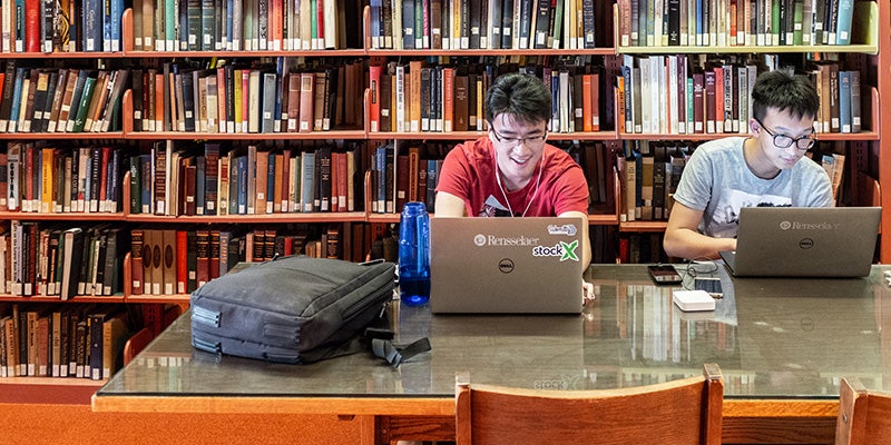 Two RPI students working on computers in the library, collaborating on research and academic projects in a focused study environment.