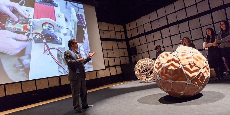 Professor poses in front two round sculptures with large display in back