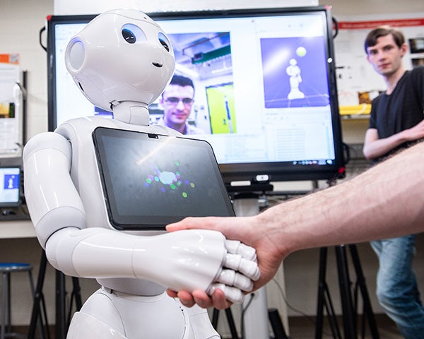 RPI student shakes hand with robot they are working within a lab