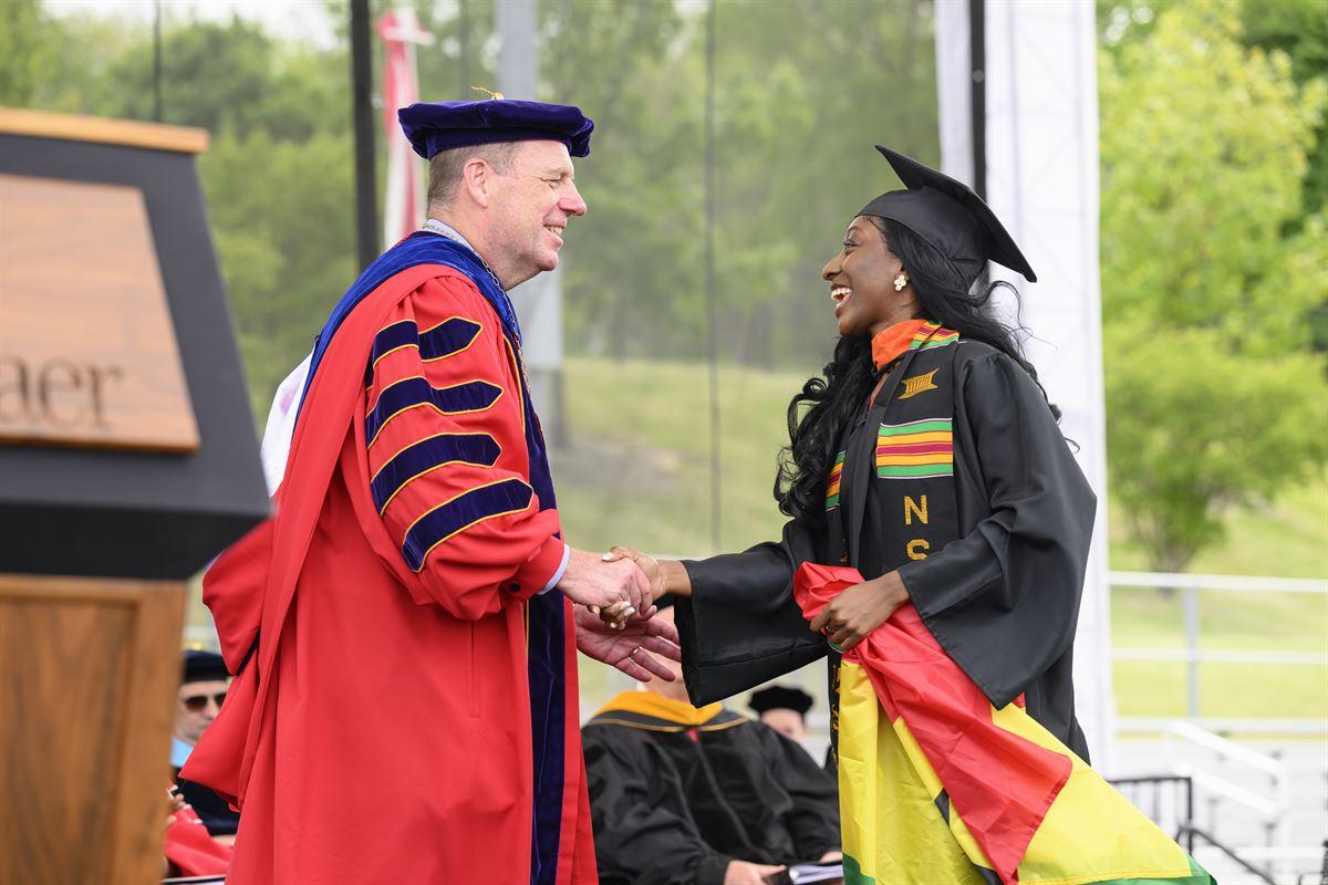 President Schmidt shakes hand with undergraduate female student crossing stage.