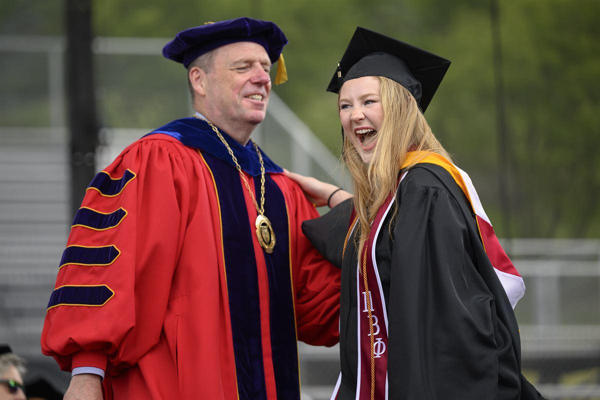 President Schmidt laughs with undergraduate female student crossing stage.