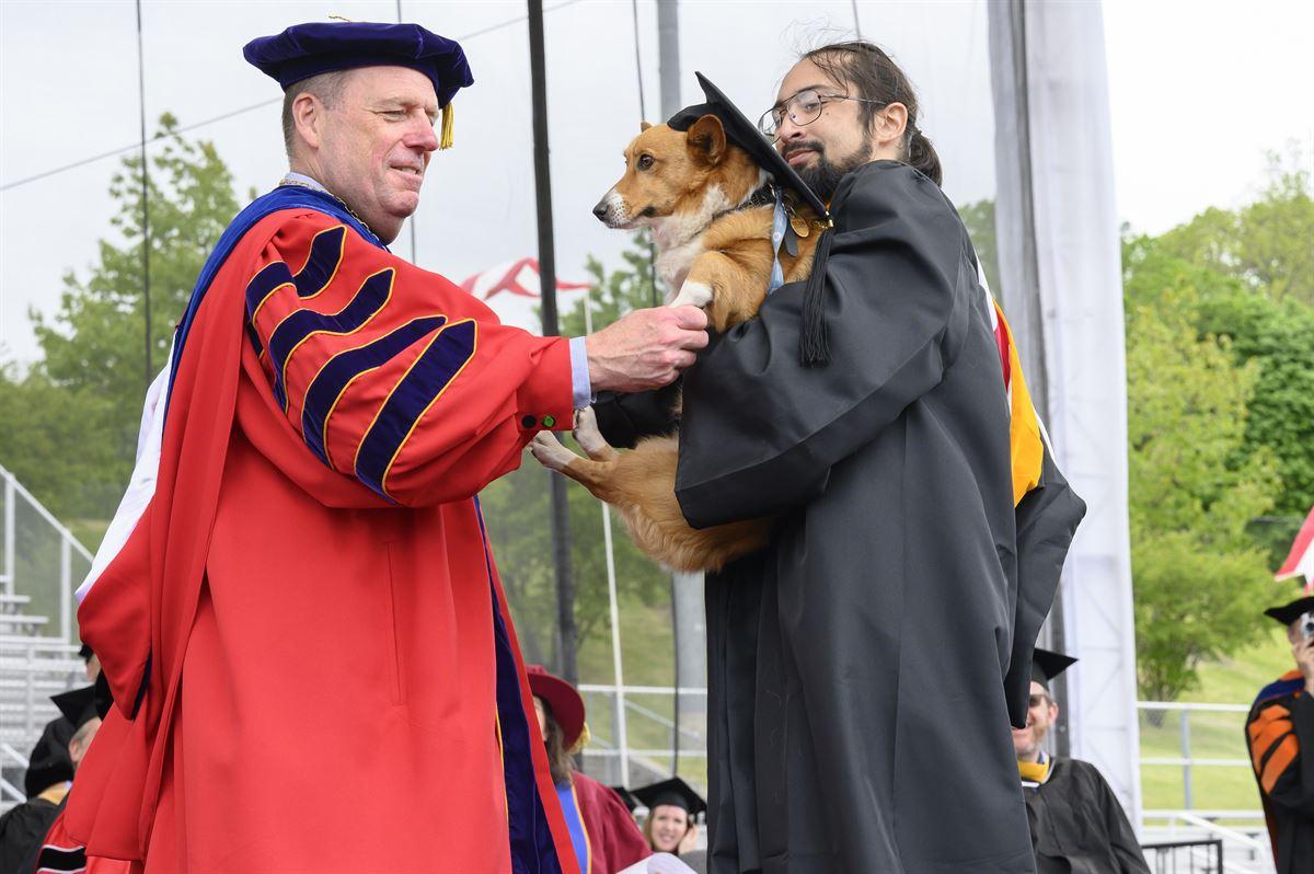 President Schmidt shakes hands with undergraduate male student and shakes his dog’s paw.