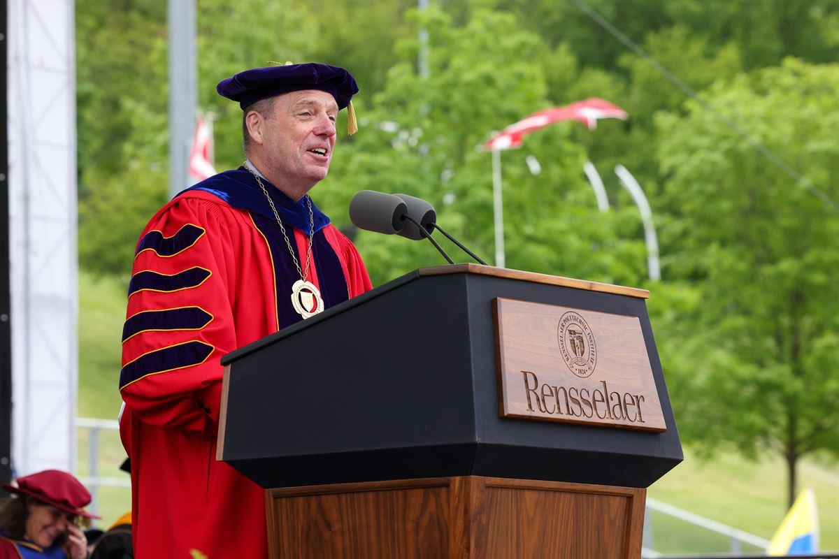 President Marty Schmidt smiles and speaks at podium during Commencement.