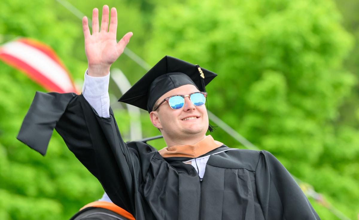 Graduate wearing sunglasses waves as he crosses the stage.