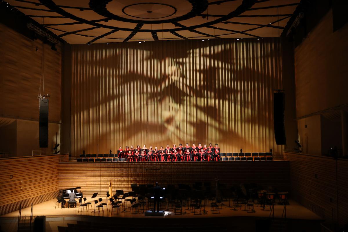 Zoomed out view of the Concert Choir performing during RPI's holiday concert. Spotlight shines on someone playing the piano.