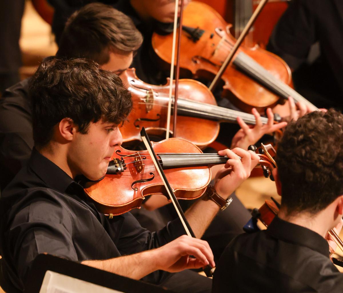 Two student musicians seated among a group in an orchestra playing violins, focusing intently on their sheet music during RPI's holiday concert.