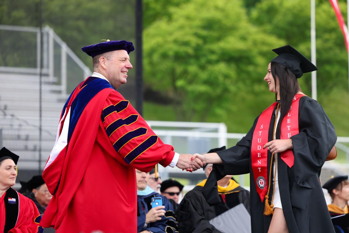 President Martin Schmidt shakes hands with a graduate who is crossing the stage.