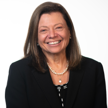 Headshot of Andrea Ballinger wearing a dark blazer and pearl necklace against a white background.