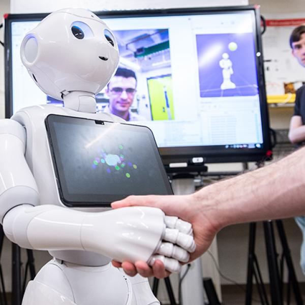 RPI student shakes hand with robot they are working within a lab